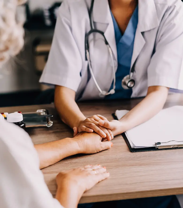 Doctor giving hope close up shot of a young female physician leaning forward to a smiling elderly lady patient holding her hand in her palms, a woman caretaker in a white coat, supporting and encouraging an old person